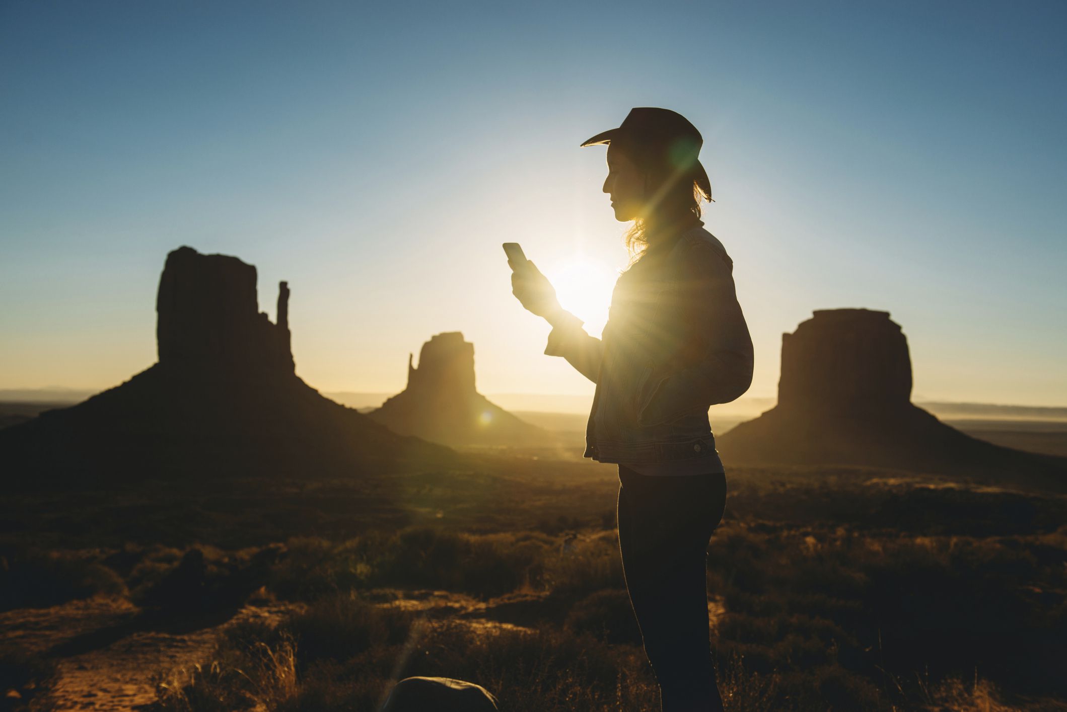 Joku käyttää älypuhelinta auringonnousun aikaan Monument Valleyssä, Utahissa. 