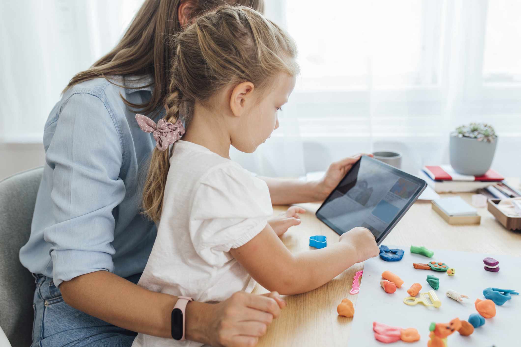 Vanhempi ja lapsi työskentelevät taidetarvikkeiden kanssa ja katsovat videota tablet-tietokoneella.