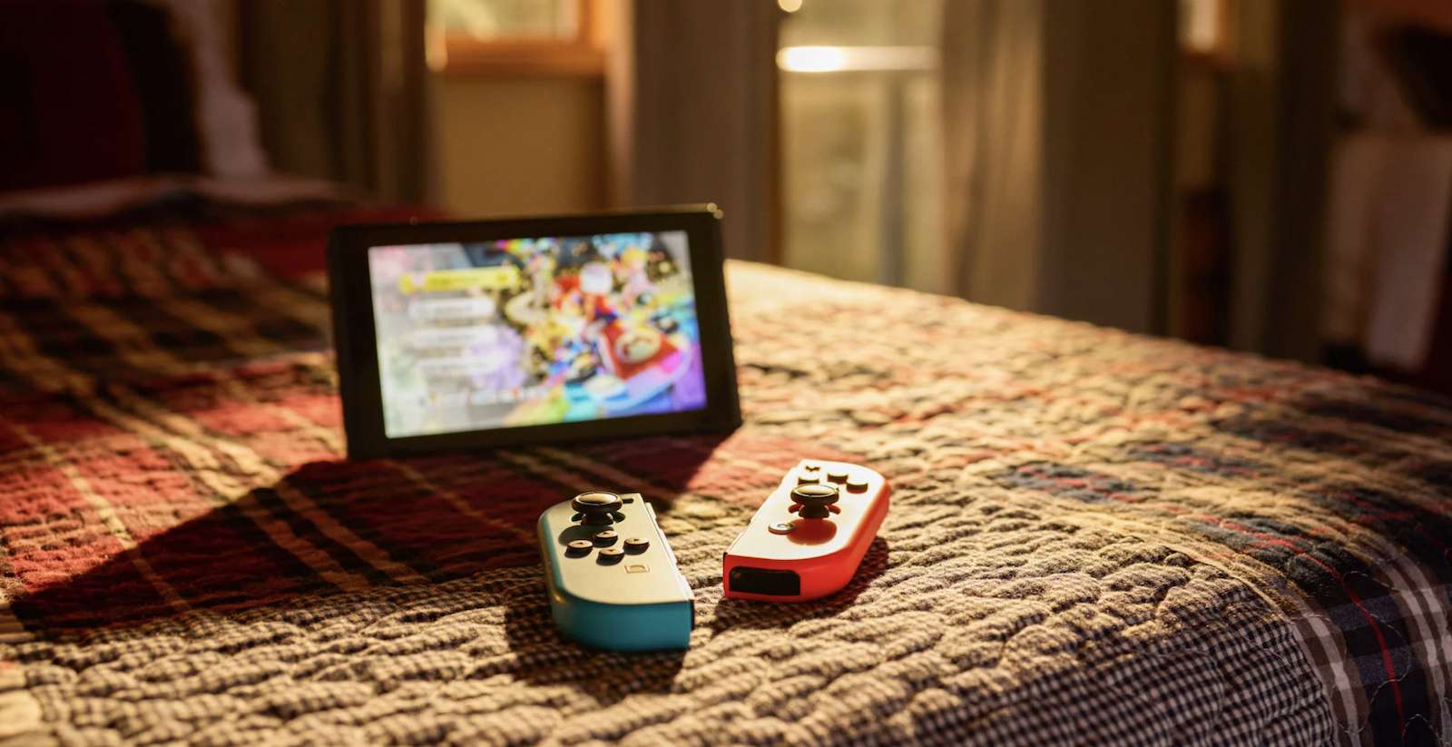 Nintendo Switch jalustalla ja Joy-Con-ohjaimilla sängyllä