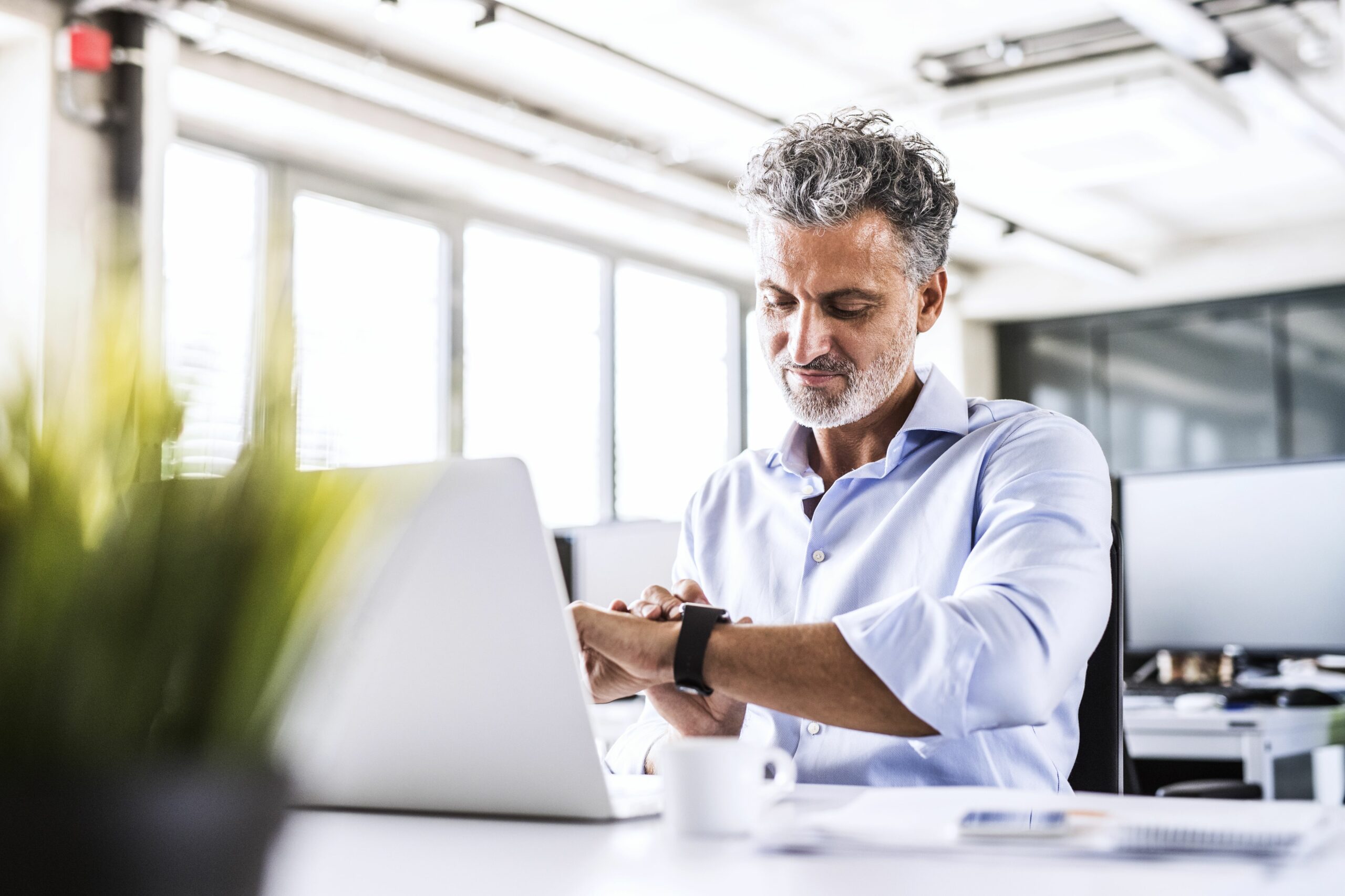 mature businessman sitting at desk in office looking at smartwatch 951529850 5b1abded8023b900366f9472 scaled