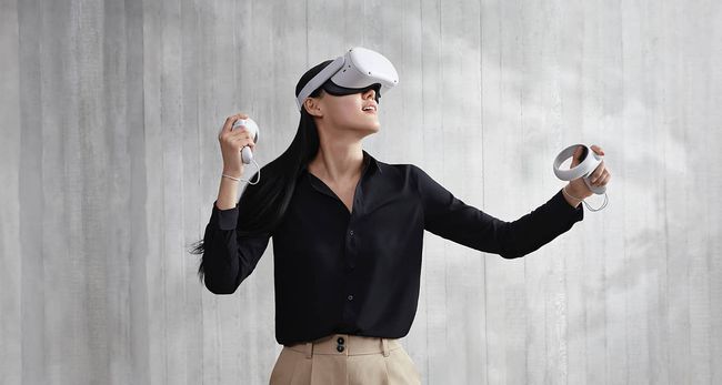 nainen käyttää Oculus Quest 2 -kuulokkeitaan harmaan seinän edessä