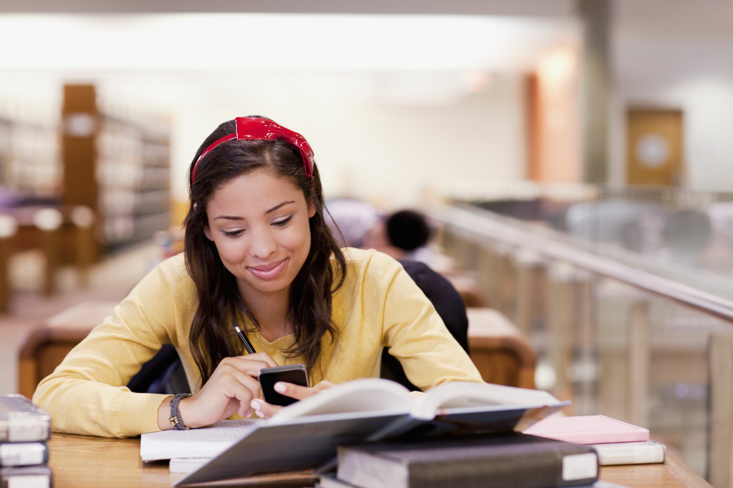 student using cell phone and studying in library 143071367 59b2bb2ab501e800145865ae scaled