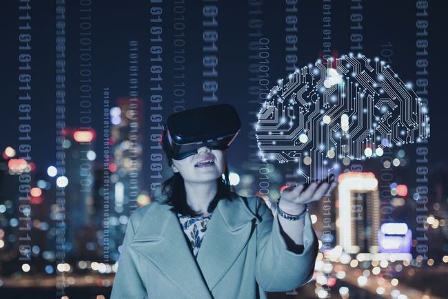 Virtuaalitodellisuuden käsitteellinen kuva VR-laseja käyttävästä henkilöstä, jonka aivot on muodostettu painetun piirilevyn valaistuksesta binäärikoodilla, joka peittää öisen vilkkaan kaupungin taustan.