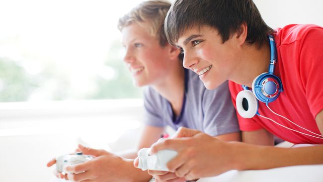 Kaksi teinipoikaa pelaamassa Xbox-videopelejä sängyllä makaamassa