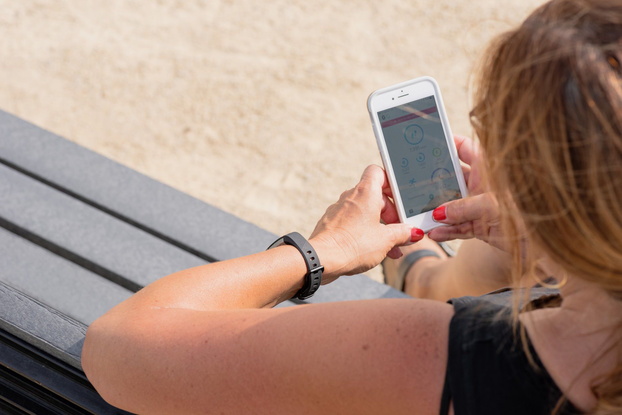 woman sitting outside on park bench checking fitbit and smartphone goal stats t20 GgYjAo a405a0b1bcf74e0eb9e33f449a2bcad7