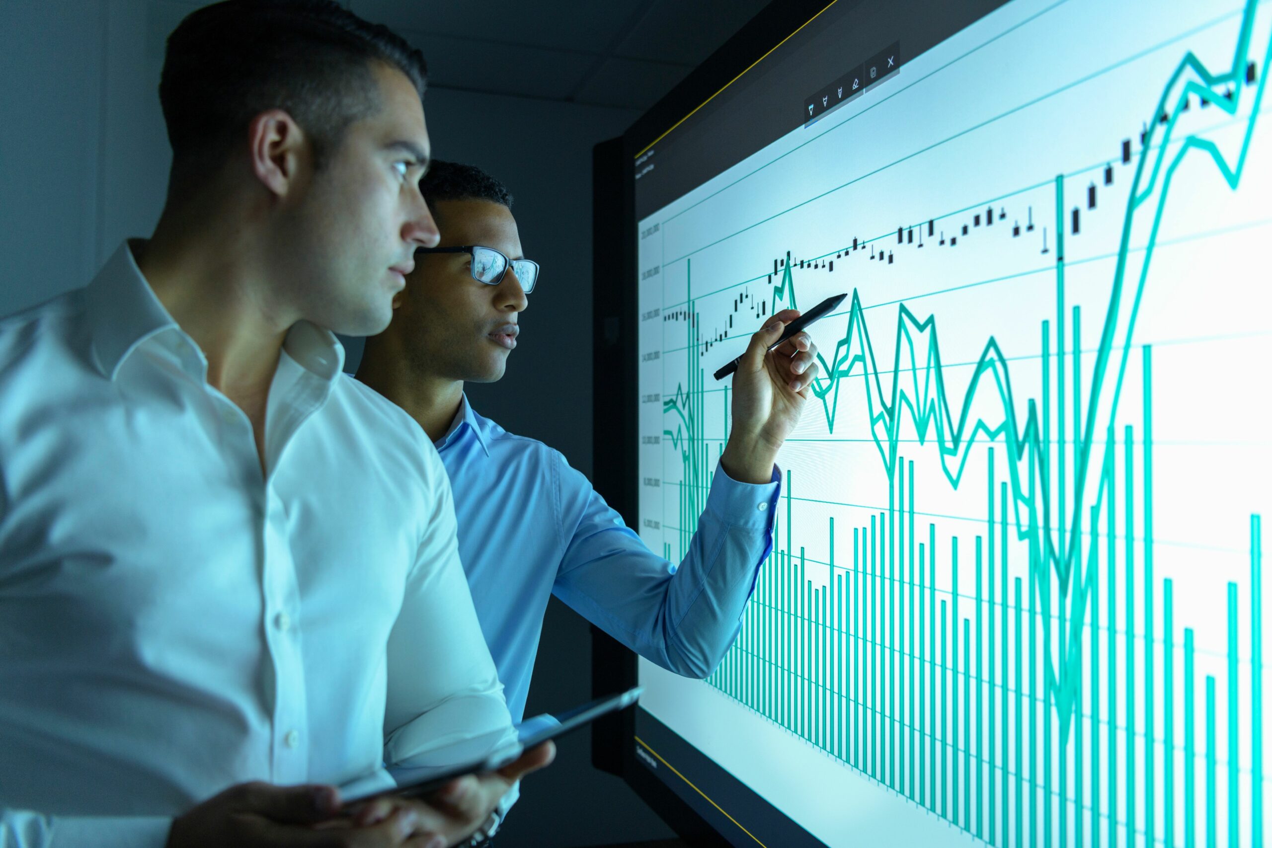 businessmen studying graphs on an interactive screen in business meeting 973708488 5bda09e946e0fb002d3ec0d3 scaled