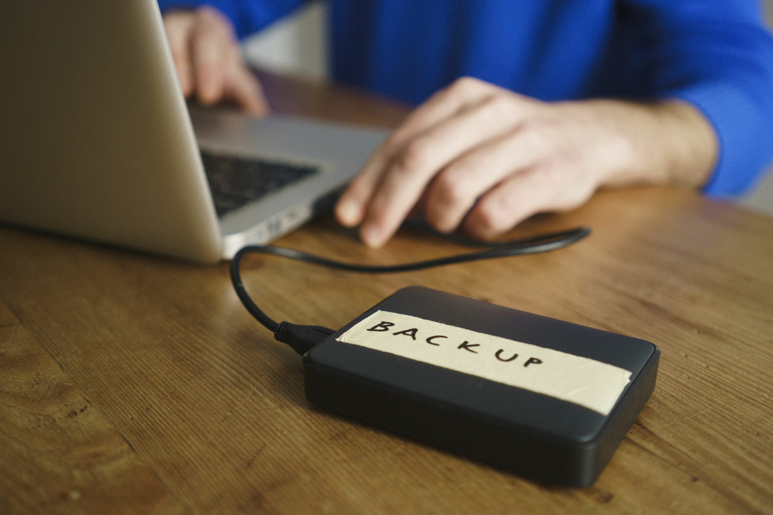 midsection of man using laptop with backup label on external hard disk drive at table 962574588 5b79f883c9e77c00572b2b8c scaled