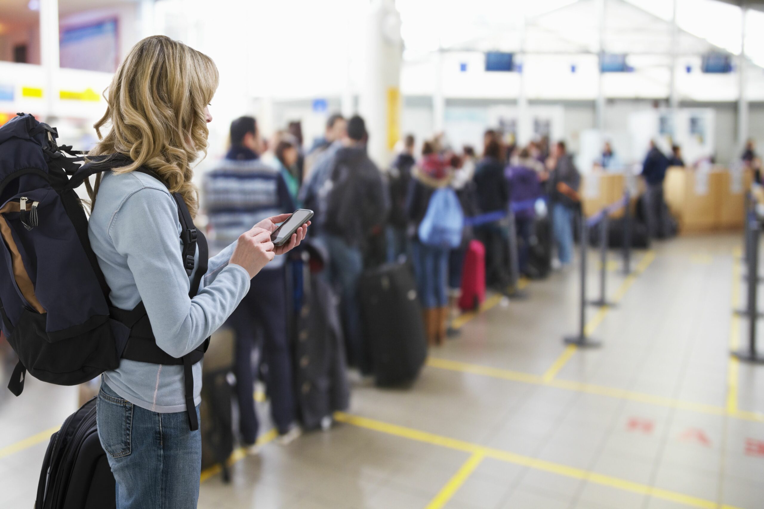 female traveller texting at airport check in desk 142309131 5a0b352813f1290037c17caf scaled