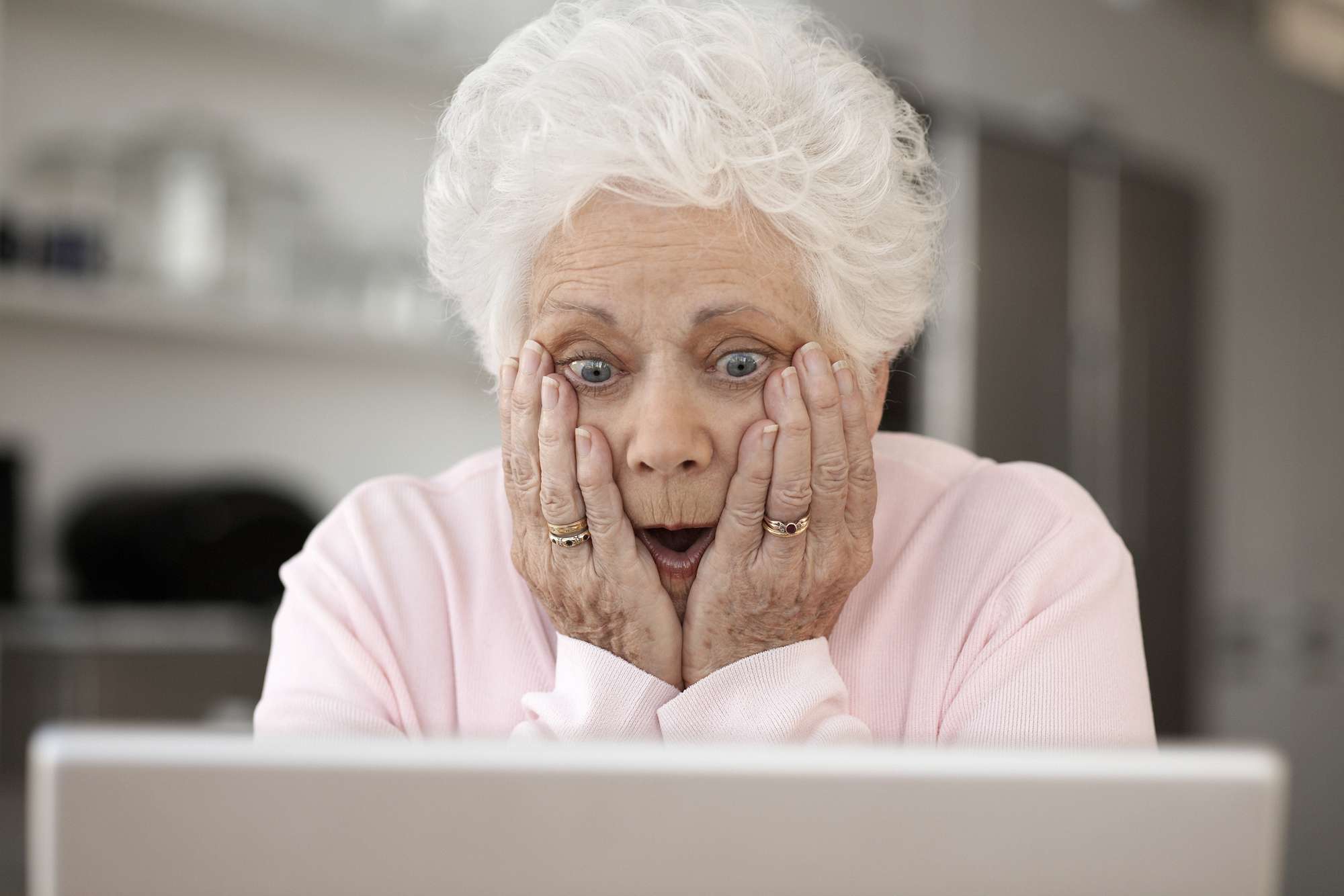 Nainen katselee kannettavaa tietokonetta pää käsissä ja suu auki
