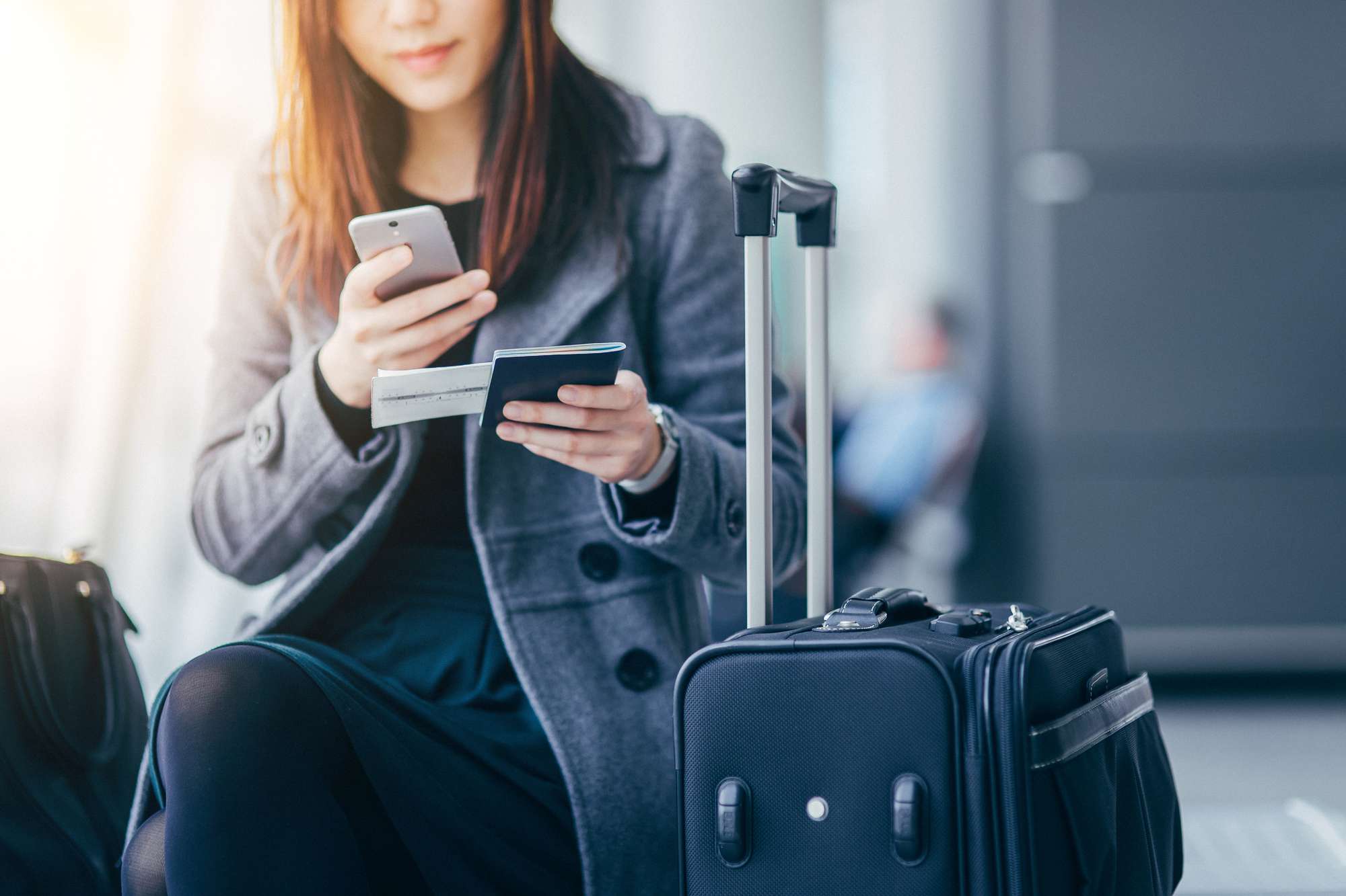 Nainen älypuhelimella ja passilla lentokentällä